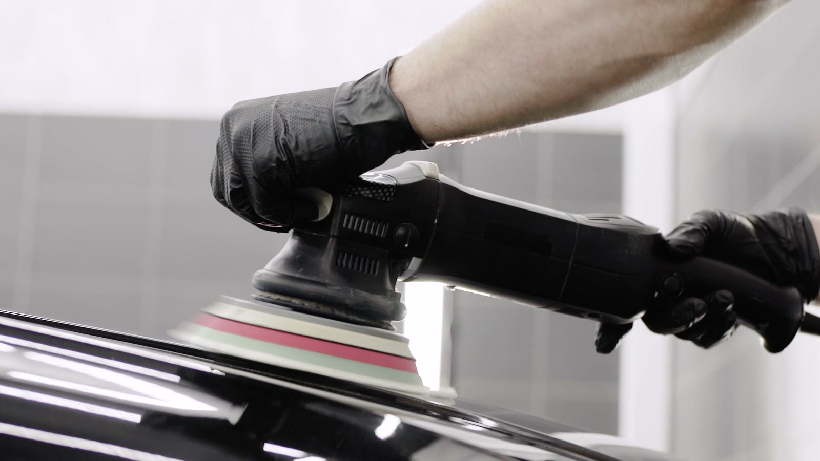 Gloved hands working a black panel with a polisher