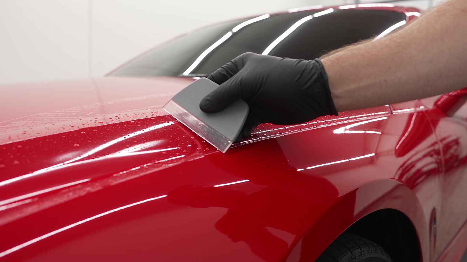 Paint protection film being squeegeed onto a red fender