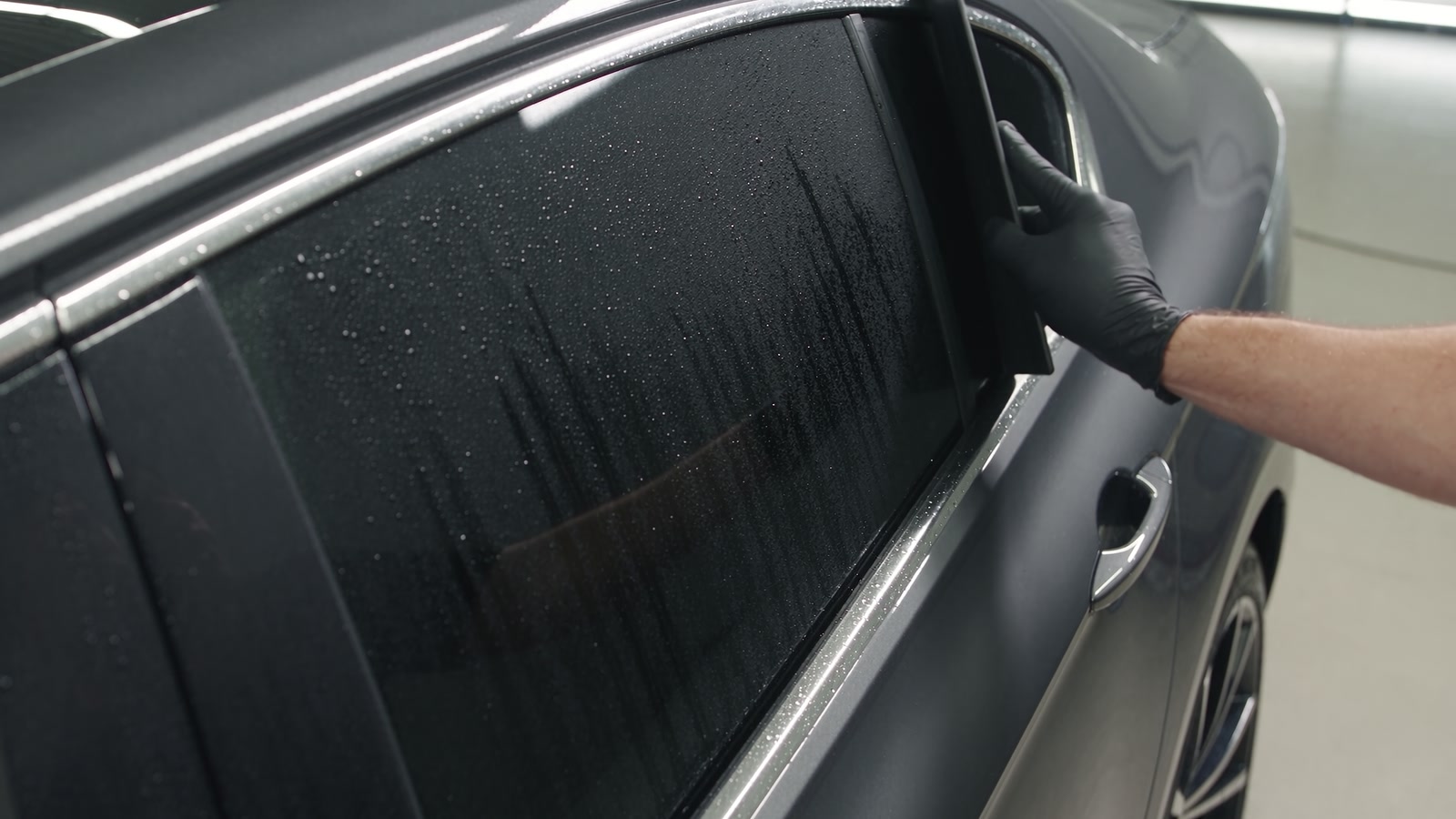 Tint film being squeegeed onto a gunmetal sedan window